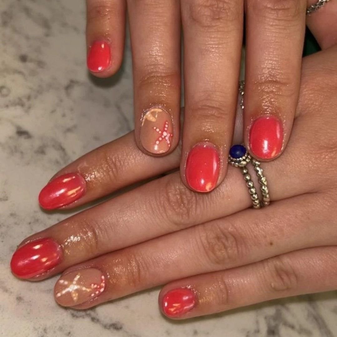 Hands with coral-colored nail polish. One nail per hand has a nude base with glittery design.