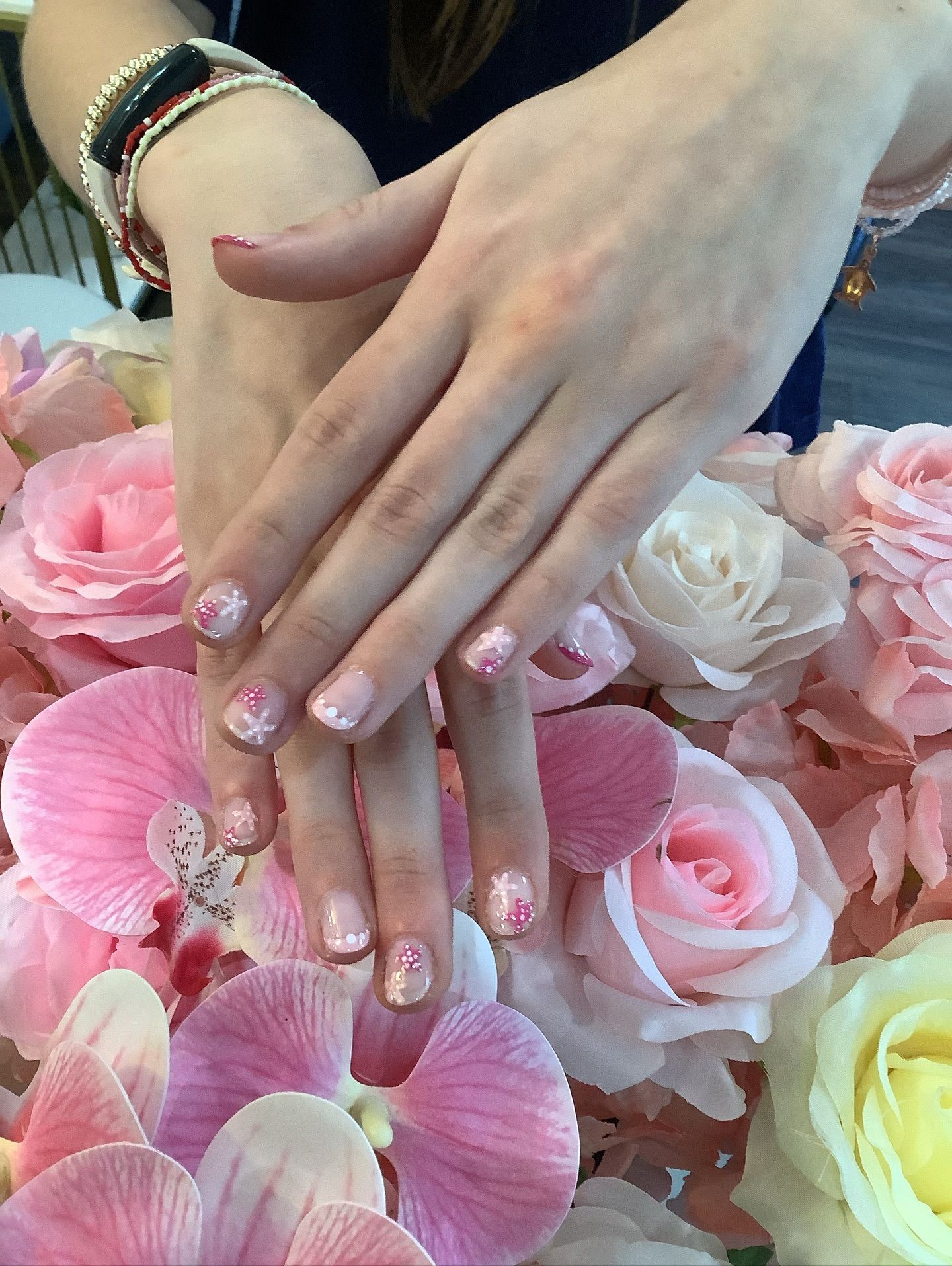 Hands with floral nail art, resting over pink flowers.