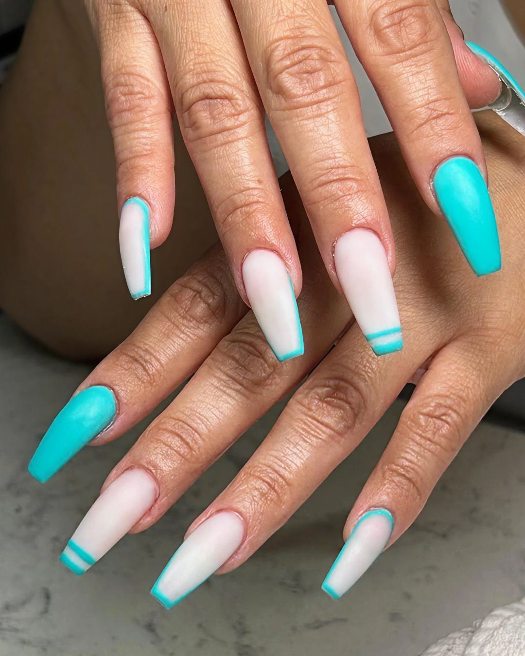 Hands with long coffin-shaped nails. Some are white with blue trim, others are solid turquoise.