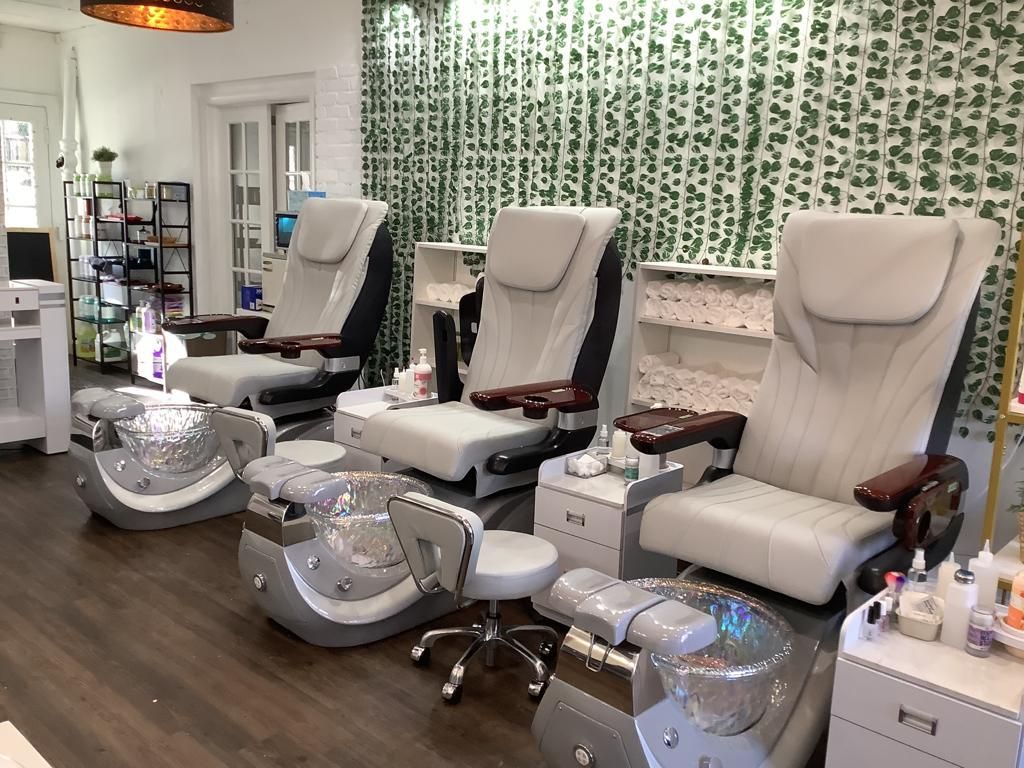Three pedicure chairs in a nail salon with a decorative wall of hanging vines.