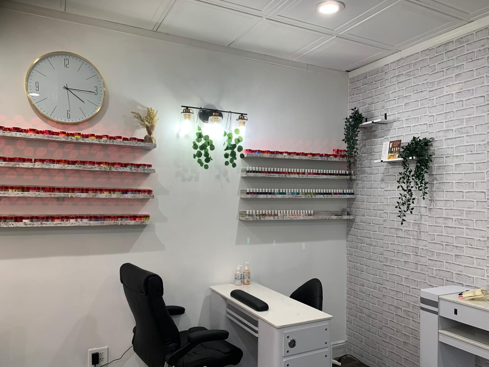 Nail salon interior with nail polish shelves, a manicure table, a clock, and decorative plants.