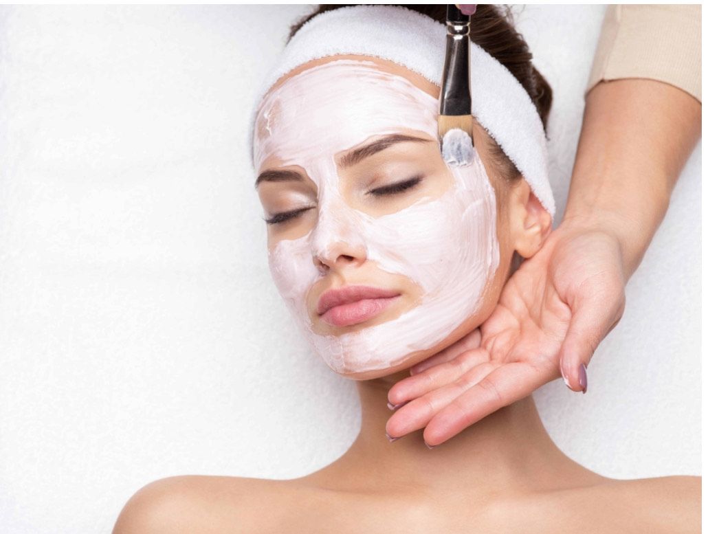 Woman with closed eyes receiving facial treatment, mask applied with brush.