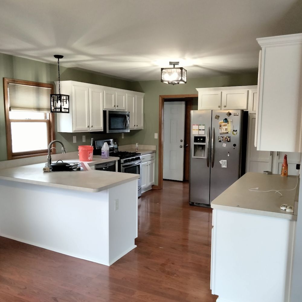 White kitchen with stainless steel appliances, light countertops, and green walls.