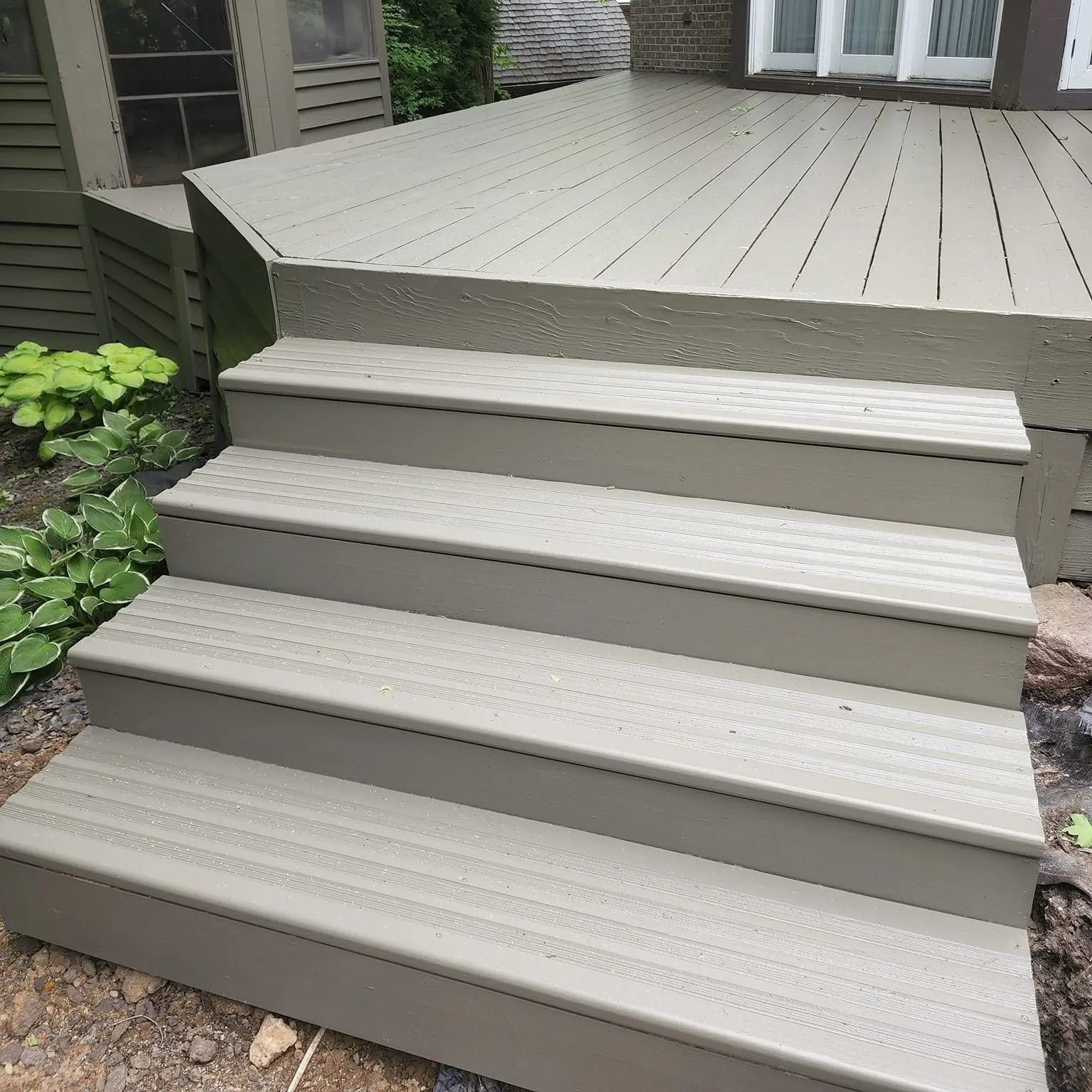 Gray composite deck and stairs leading down to a garden area with green plants.