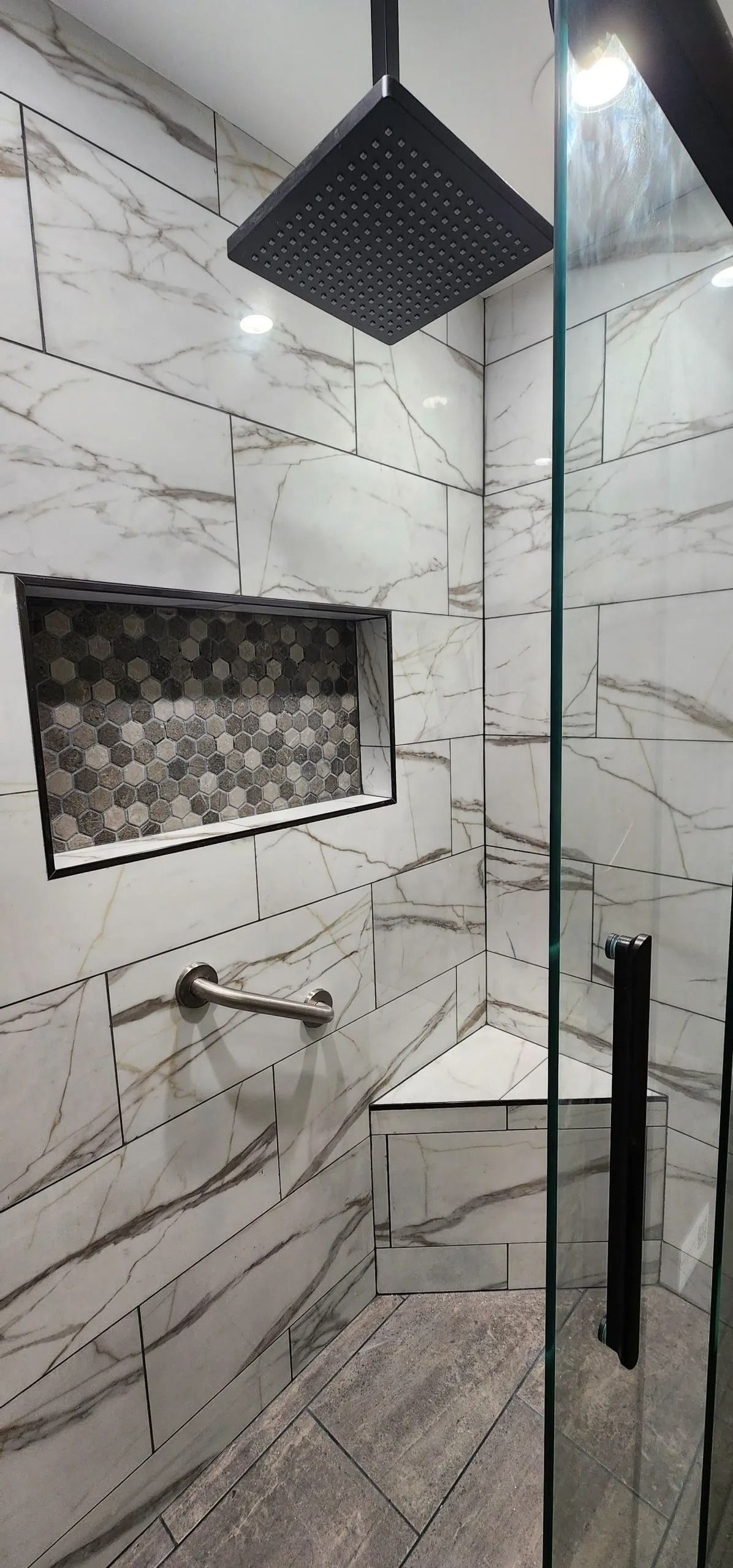 Modern tiled shower with a glass door, built-in bench, and rain shower head.
