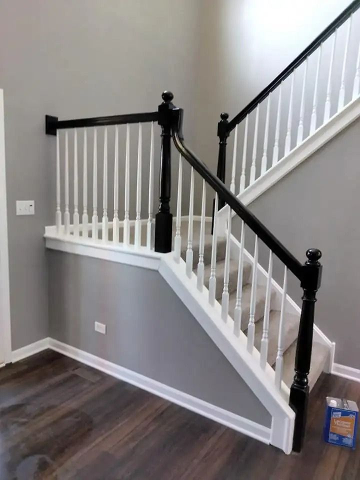 Staircase with white balusters, black posts, and gray walls. Dark wood floor.