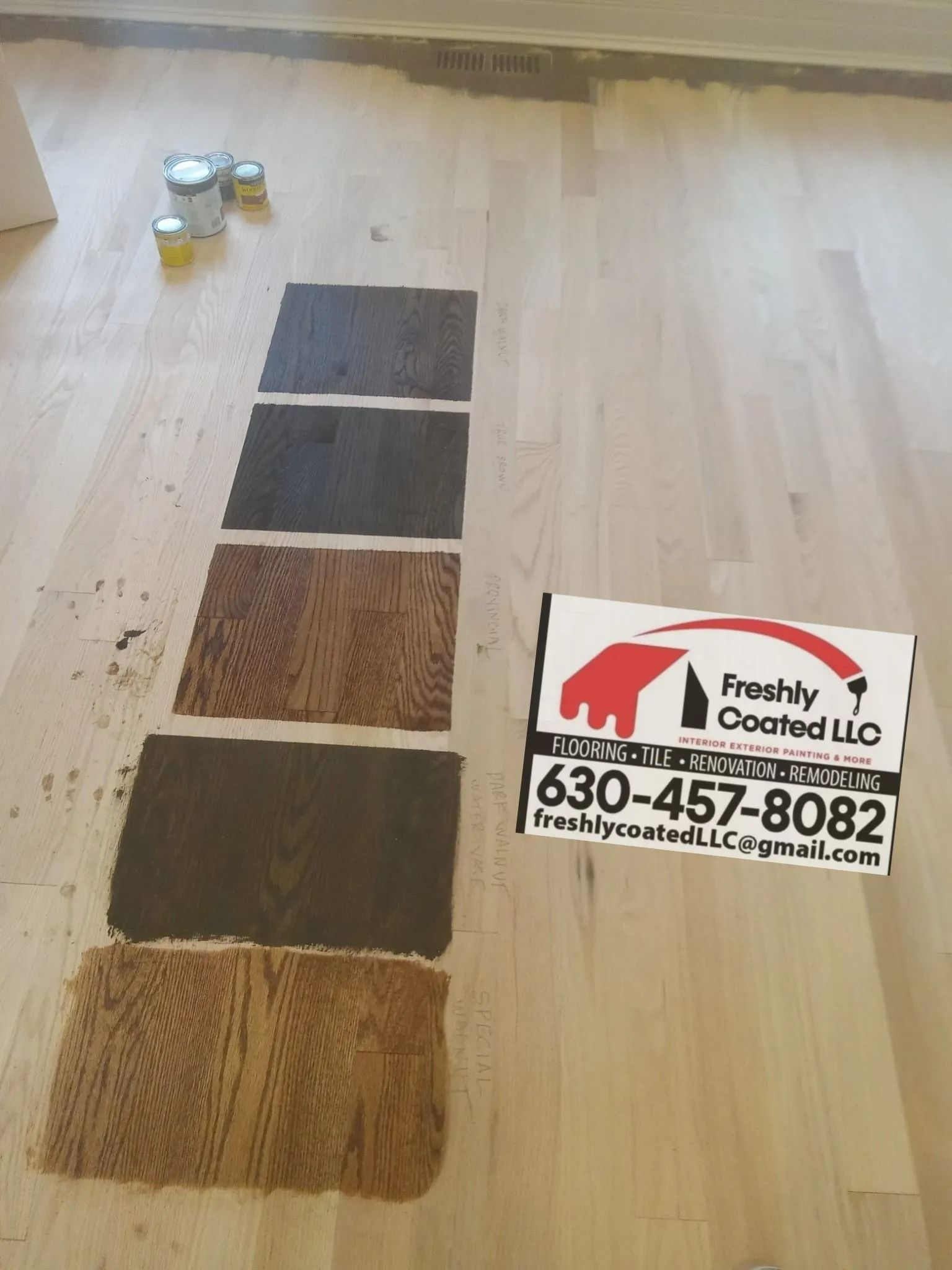 Floor samples of wood stain colors are applied on a hardwood floor. A business card with contact details rests beside the samples.
