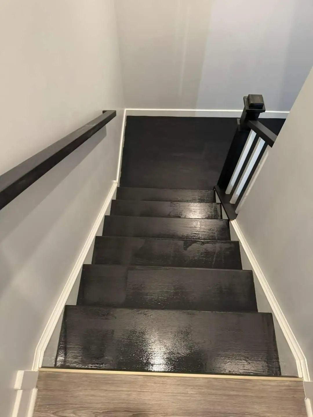 Staircase with black steps, white trim, gray walls, and black handrails.