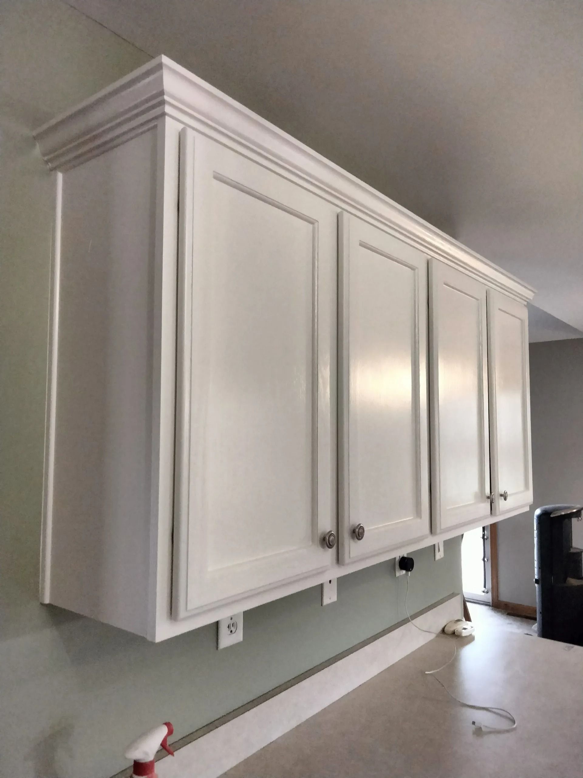 White kitchen cabinets with crown molding against a light green wall.