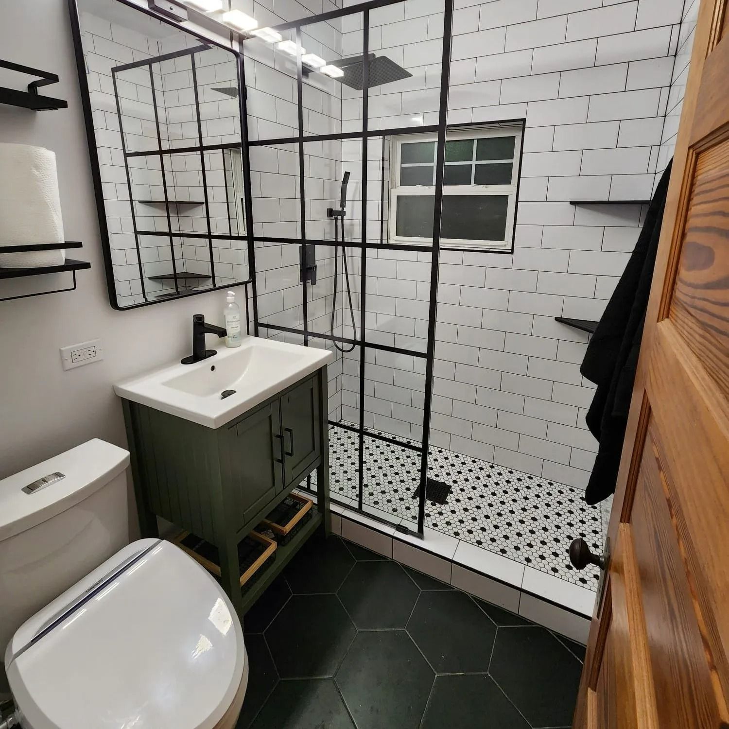 Bathroom with green vanity, black-framed shower, white subway tile, and hexagon floor tile.