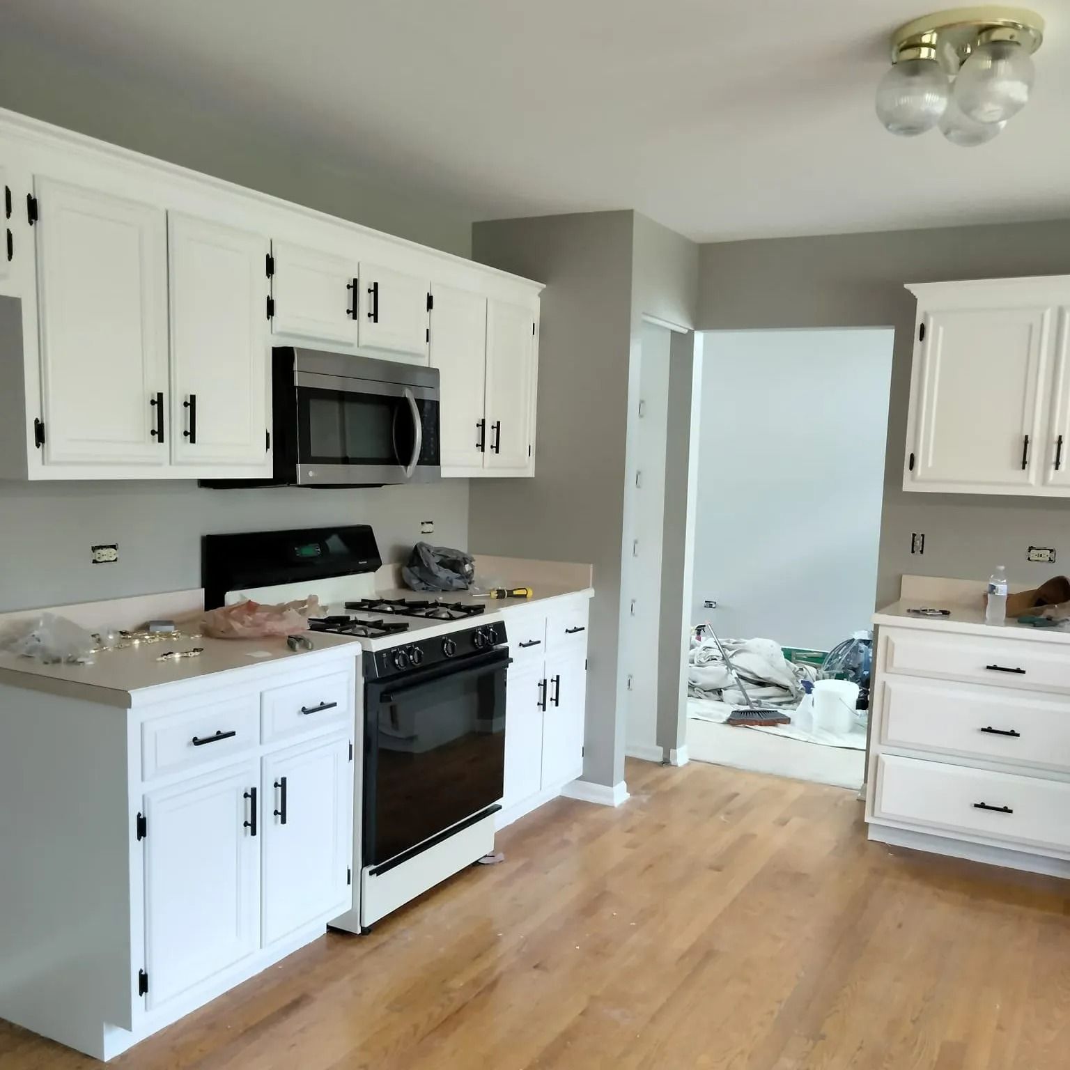 White kitchen cabinets with black hardware and appliances, gray walls, and light wood floors.