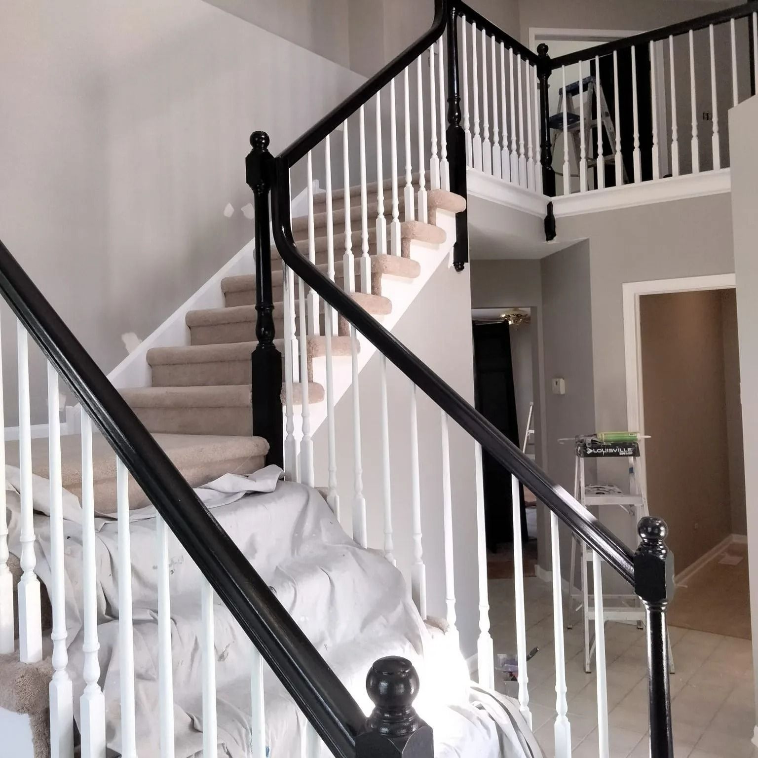 Staircase with black banisters, white spindles, and tan carpet steps. Gray walls, and a view into a hallway.
