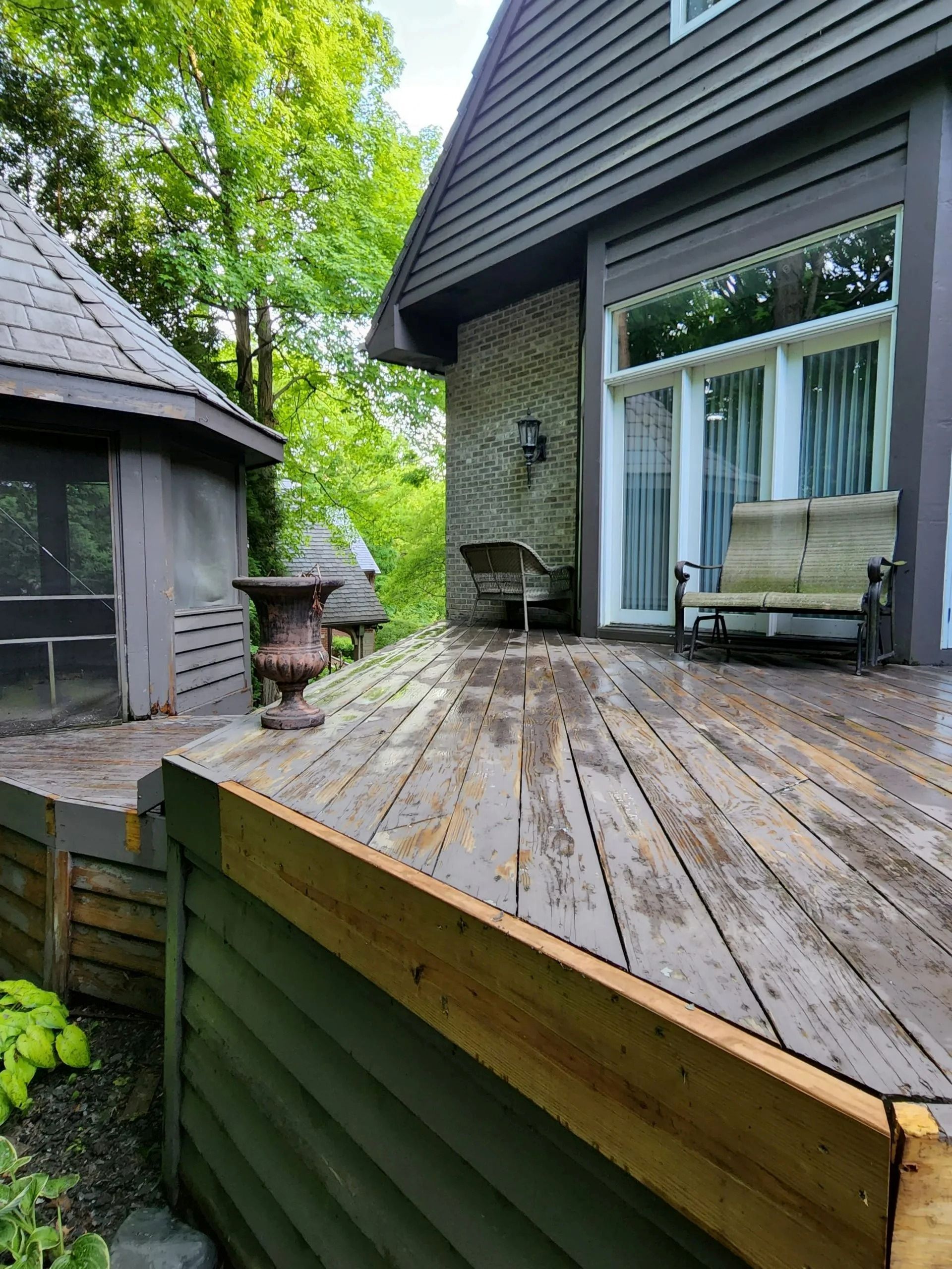 Wooden deck with weathered planks, part of a house with a gazebo in the background.