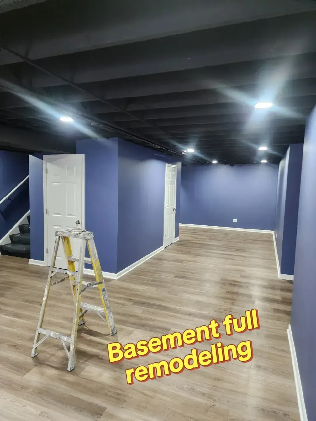 Basement undergoing full remodel; blue walls, black ceiling, tan floor, ladder present.
