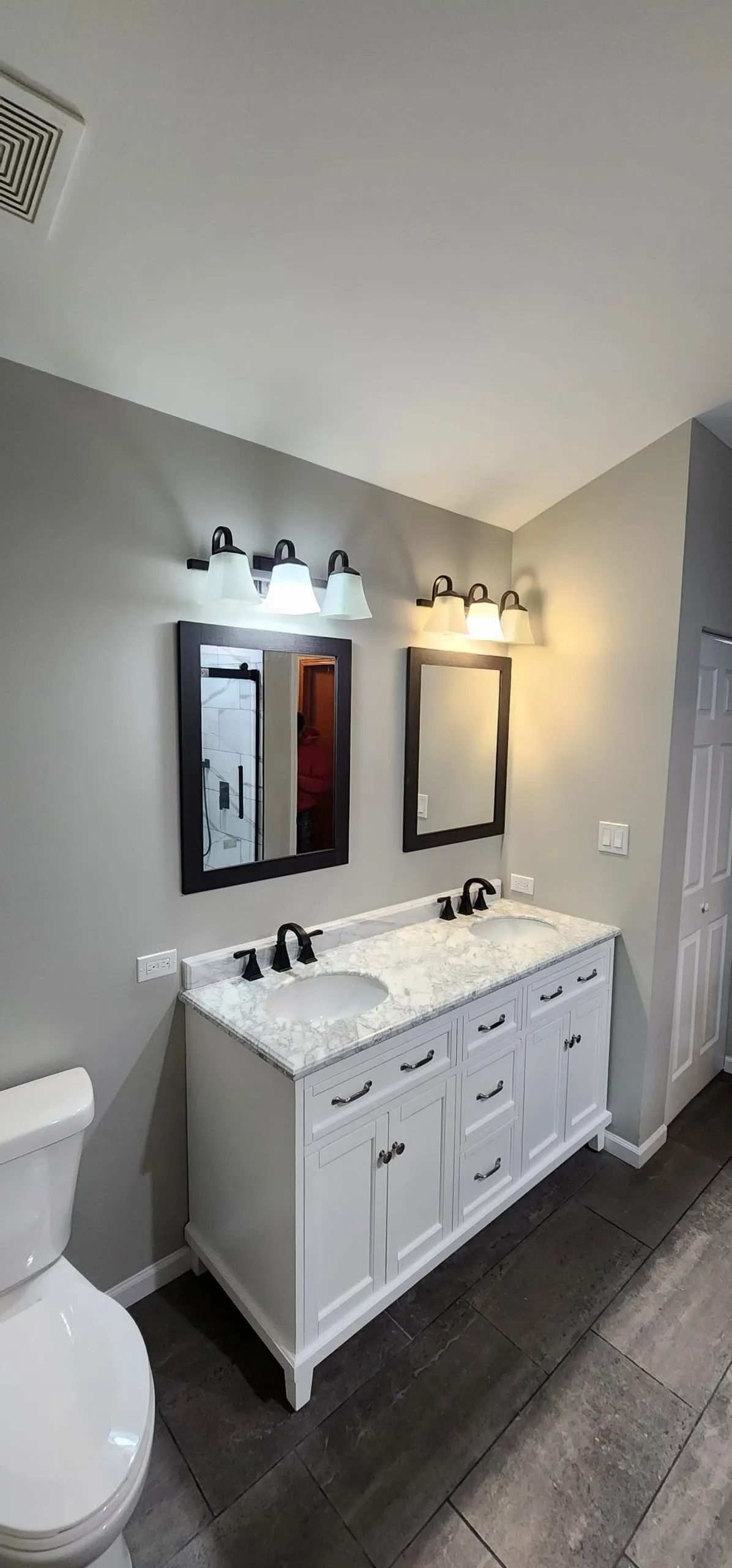 Bathroom with white double vanity, gray walls, and dark gray floor tiles.