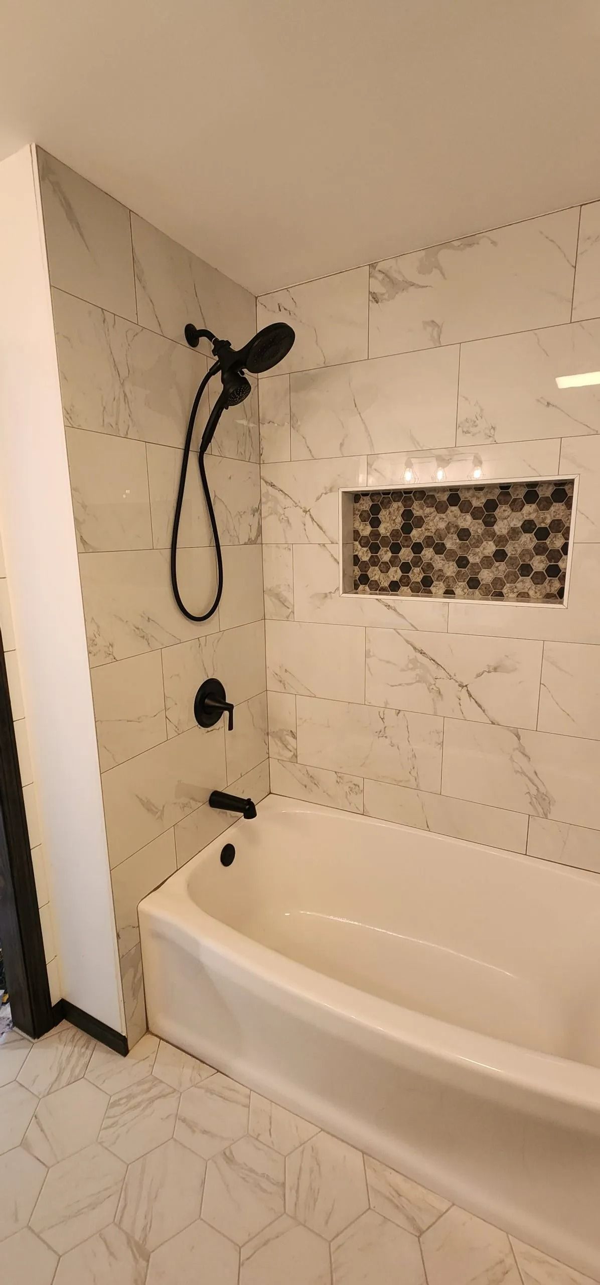 Bathroom with a white bathtub, black shower fixtures, and marble-look tile walls.