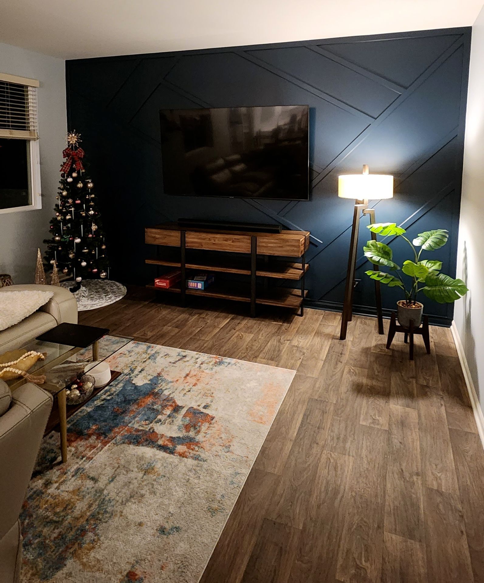 Living room with dark blue accent wall, TV, wooden console, floor lamp, rug, and Christmas tree.