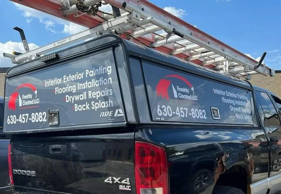 Black Dodge truck with a ladder on top; has company logo and phone number.