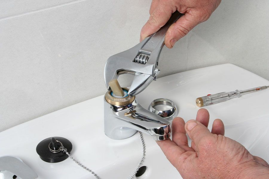 Person using a wrench to repair a chrome faucet on a white sink.