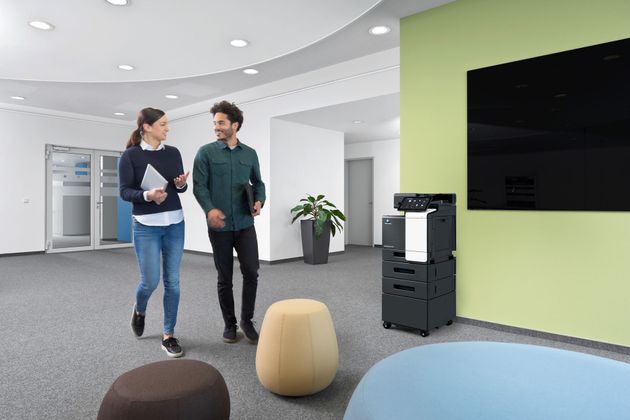 Postazione aziendale con stampante multifunzione, laptop con dashboard documentale e ambiente ufficio moderno e ordinato.