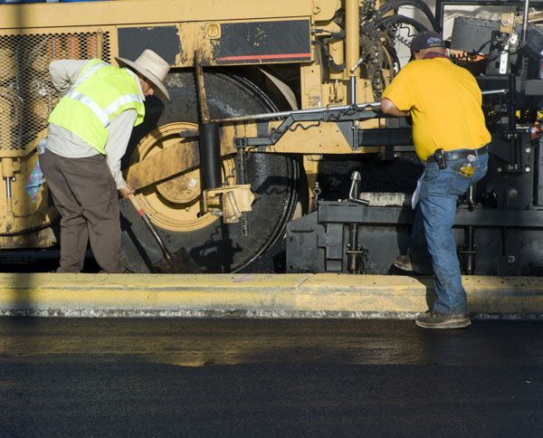 Two men are working on a road with a machine