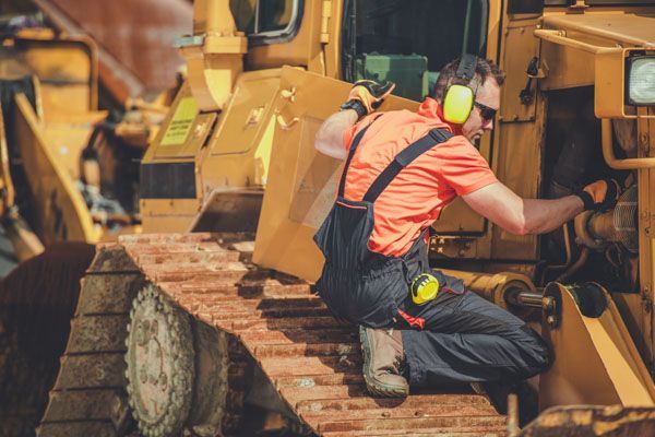 A man wearing ear muffs is working on a bulldozer.