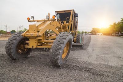 A yellow tractor is sitting on top of a dirt road.