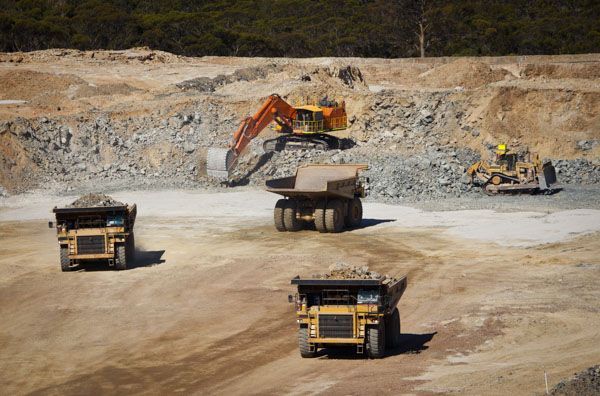 Three dump trucks are driving down a dirt road in a quarry.