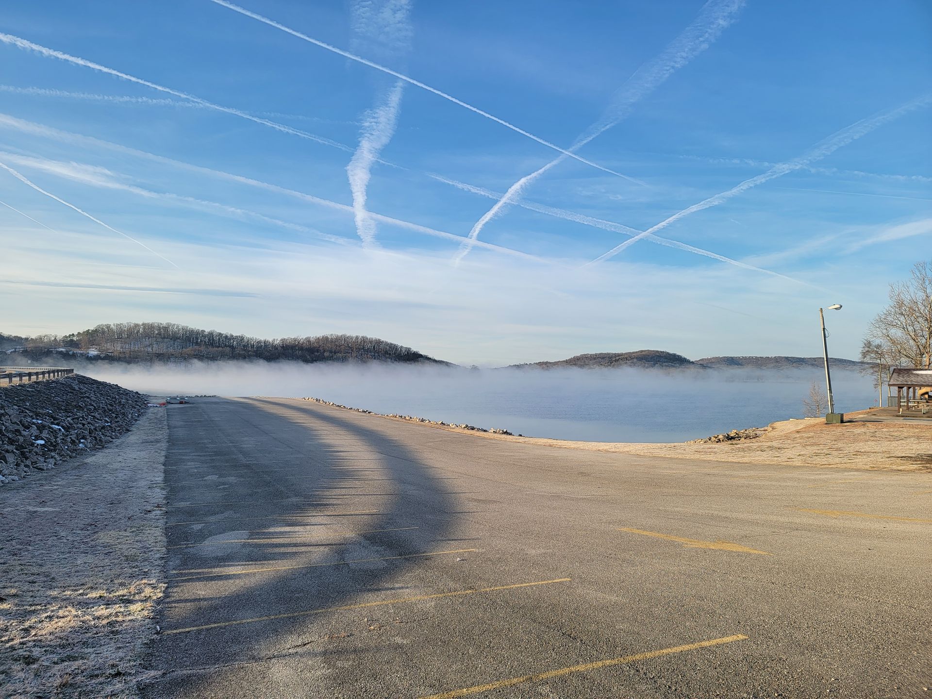 A foggy lake with a road leading to it on a sunny day.