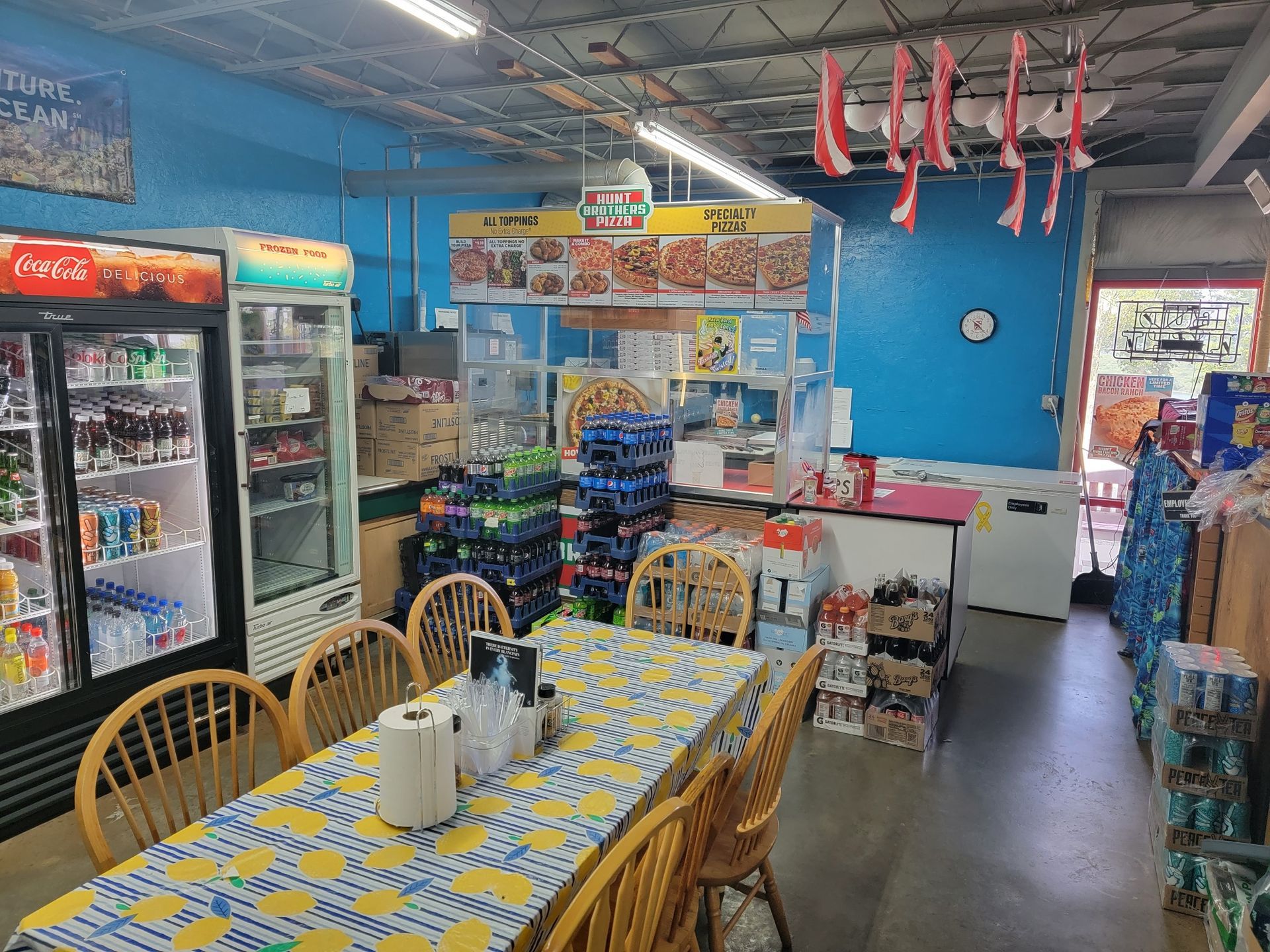 A convienence store with a long table and chairs and a coca cola refrigerator.