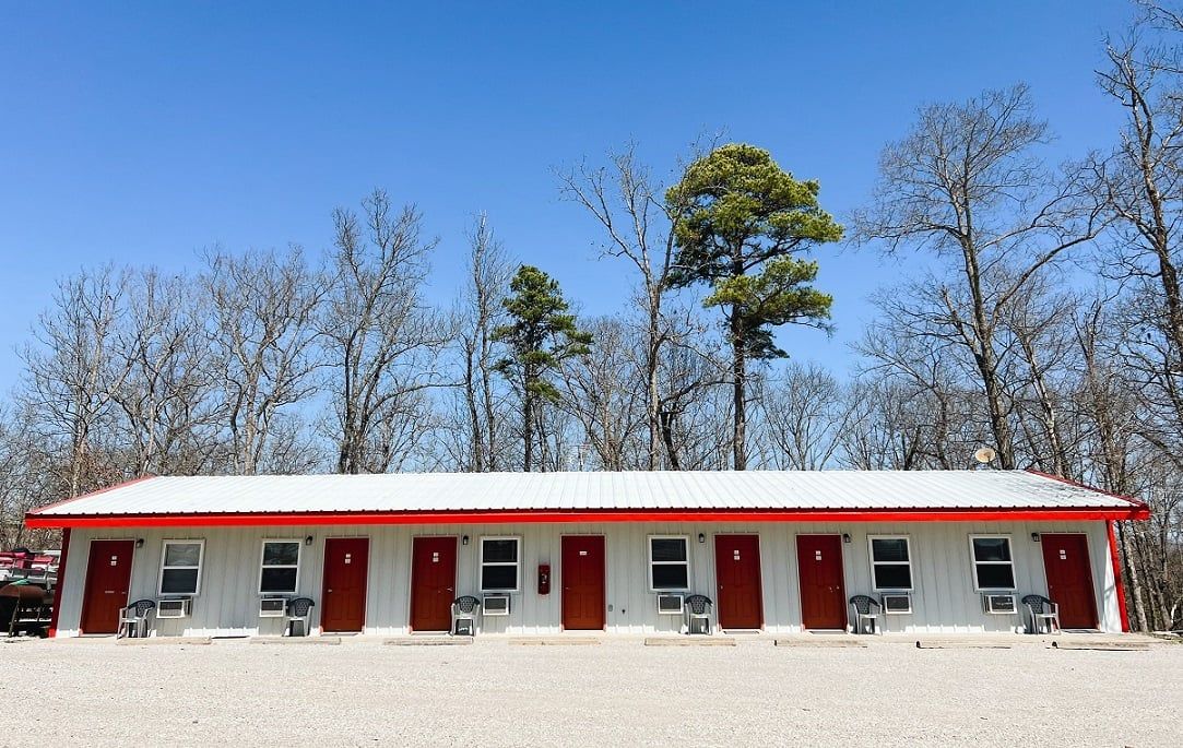 A white motel with red doors and a red roof is surrounded by trees.