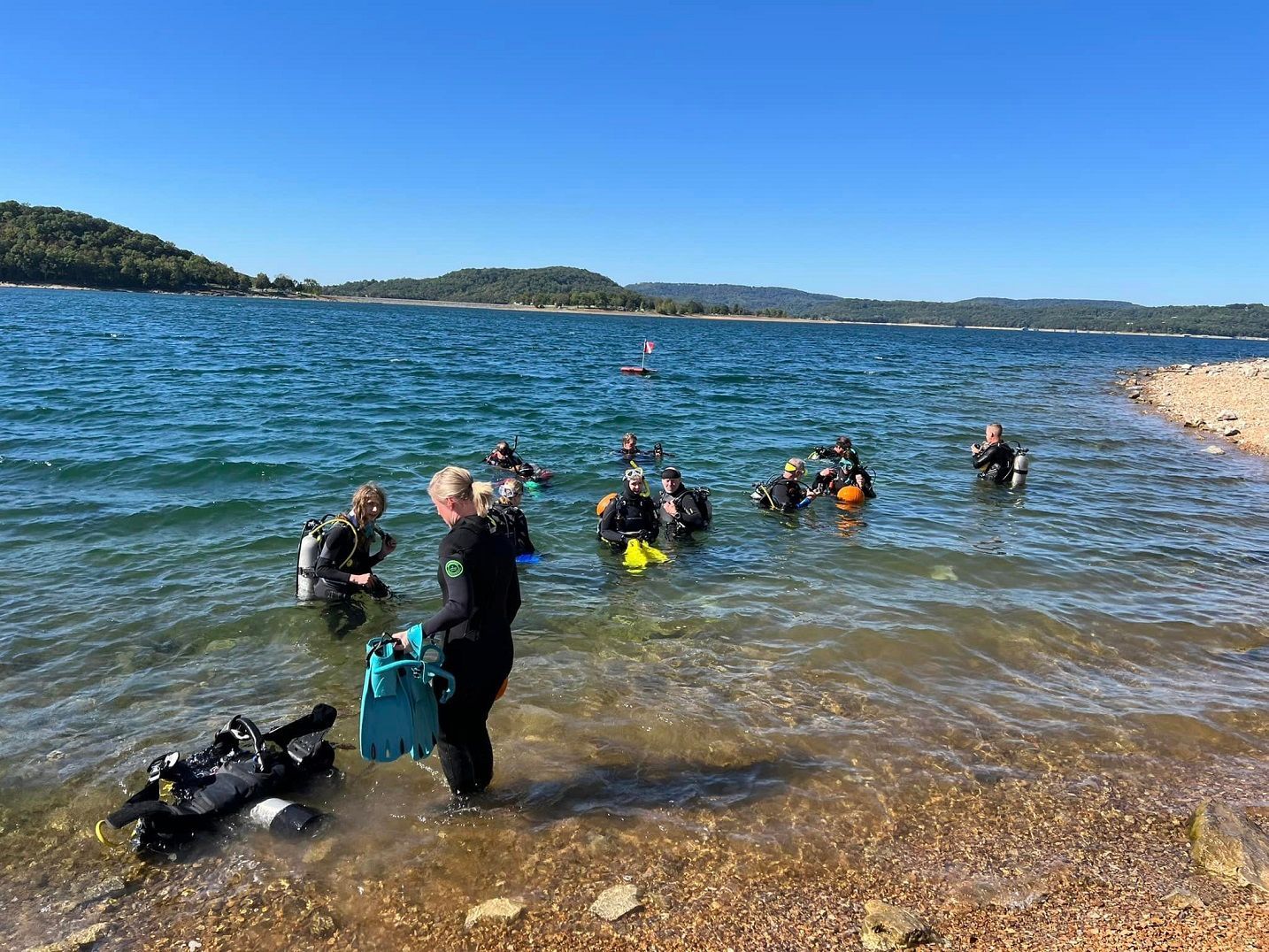 A group of people are standing on the shore of a lake.