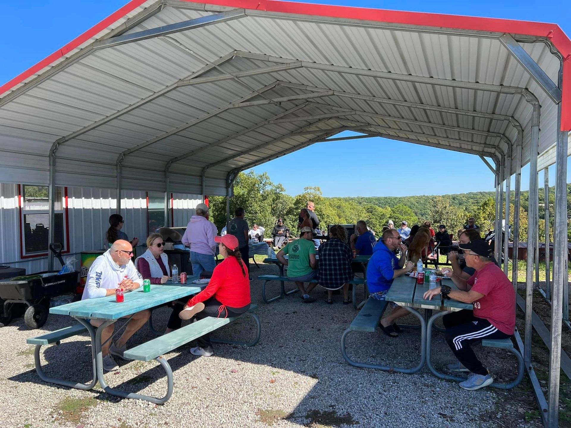 A group of people are sitting at picnic tables under a canopy.