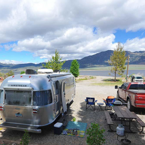A silver airstream trailer is parked next to a red truck.