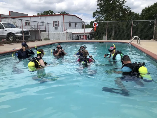 A group of scuba divers are swimming in a swimming pool.