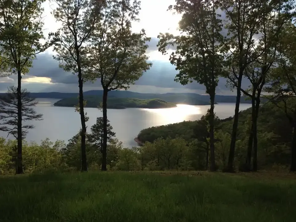 A lake surrounded by trees with the sun shining through the clouds