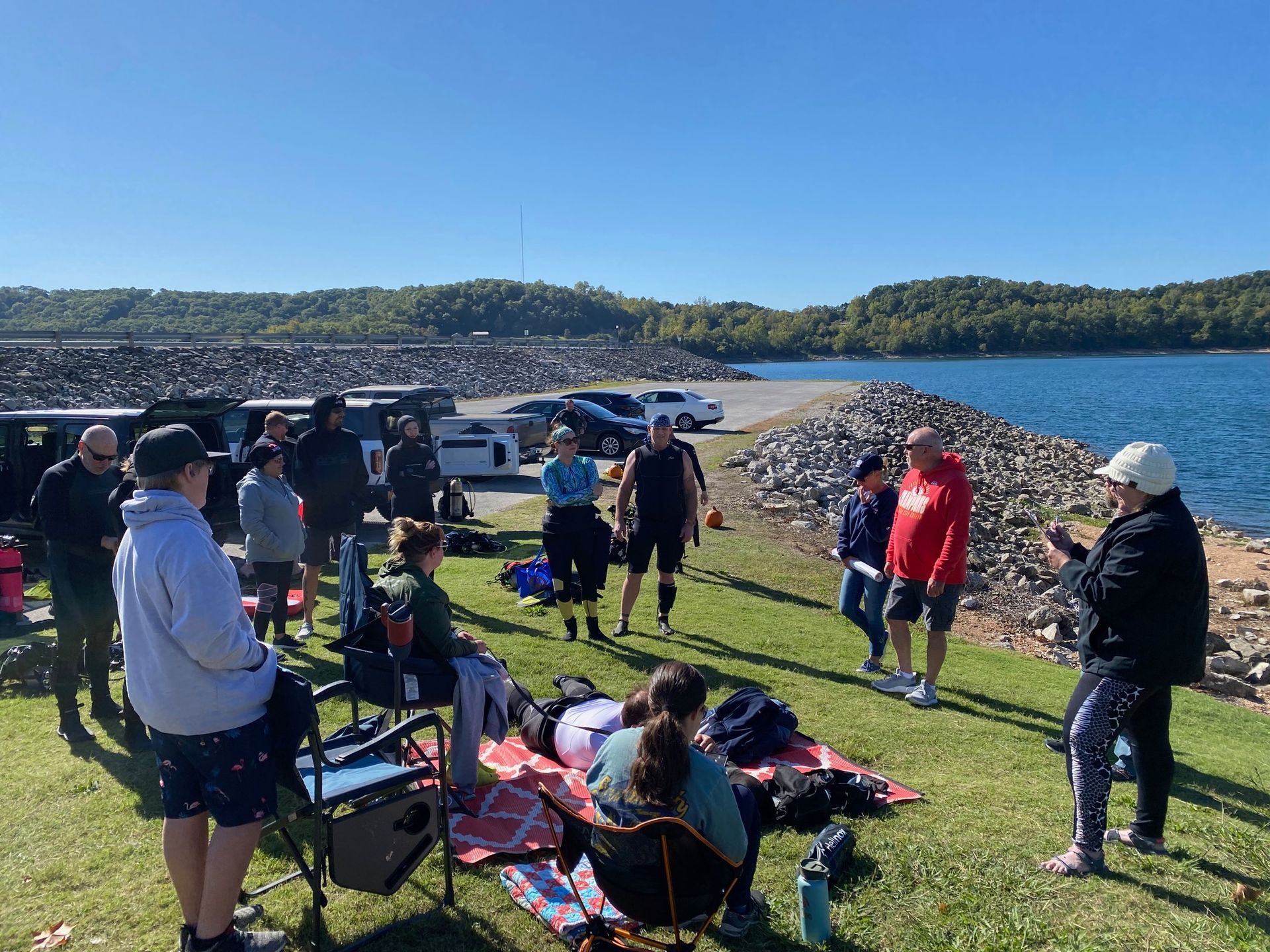 A group of people are sitting on the grass near a lake.