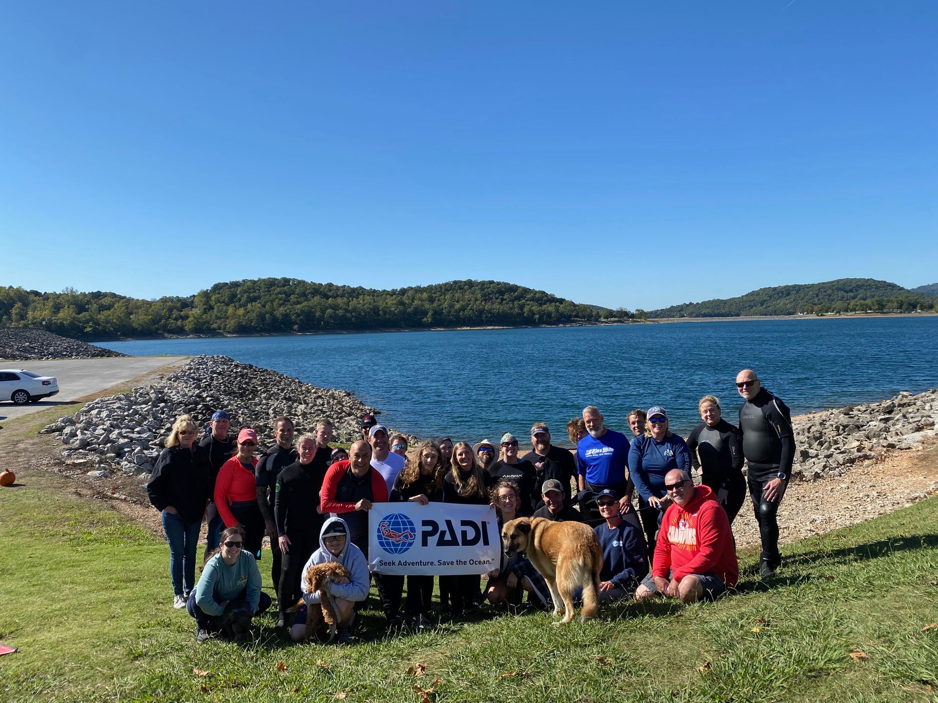 A group of people are posing for a picture in front of Beaver Lake holding a PADI sign.