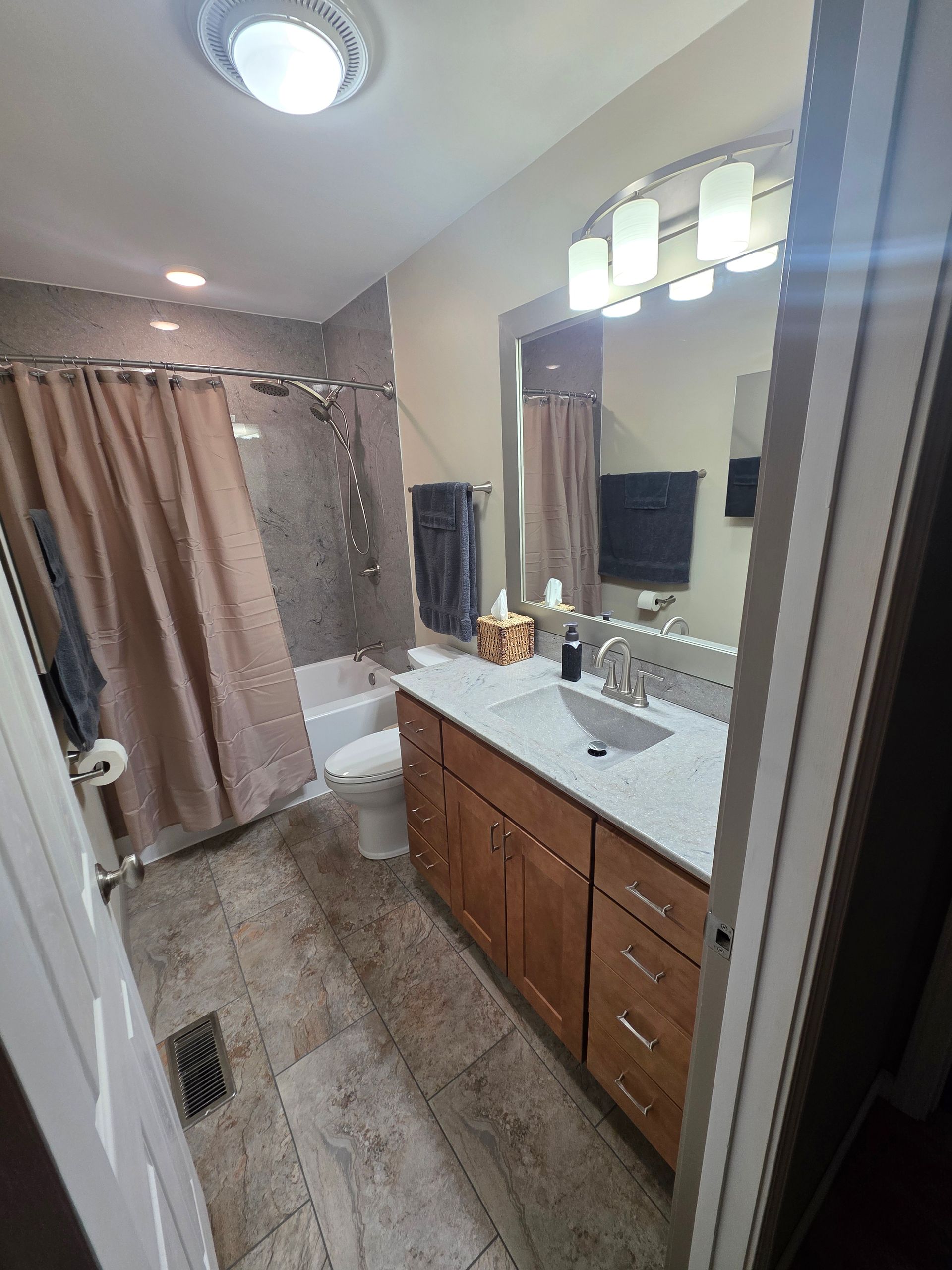 Bathroom with a vanity, toilet, and shower. Tan and gray color scheme, wood cabinets.