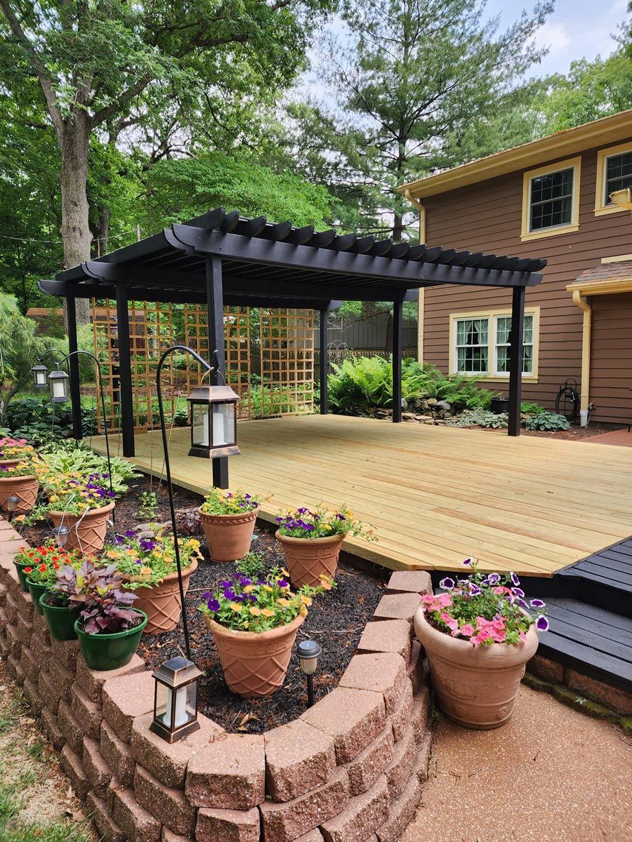 A wooden deck with a pergola and potted plants in front of a house in located Danville, IL.