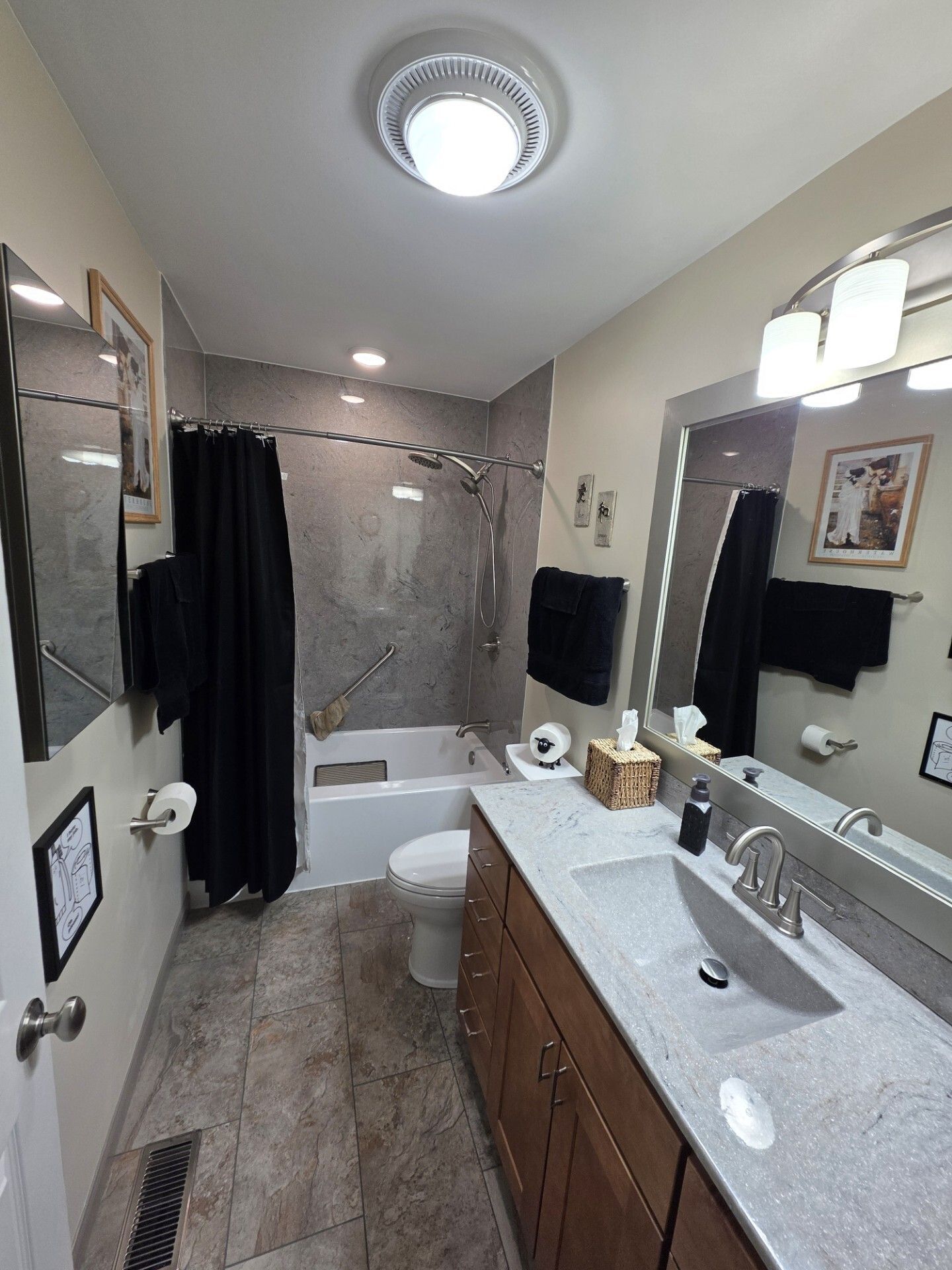 Bathroom with a long vanity, toilet, and shower/tub combo. Dark towels and curtains, light gray tile. Danville, IL