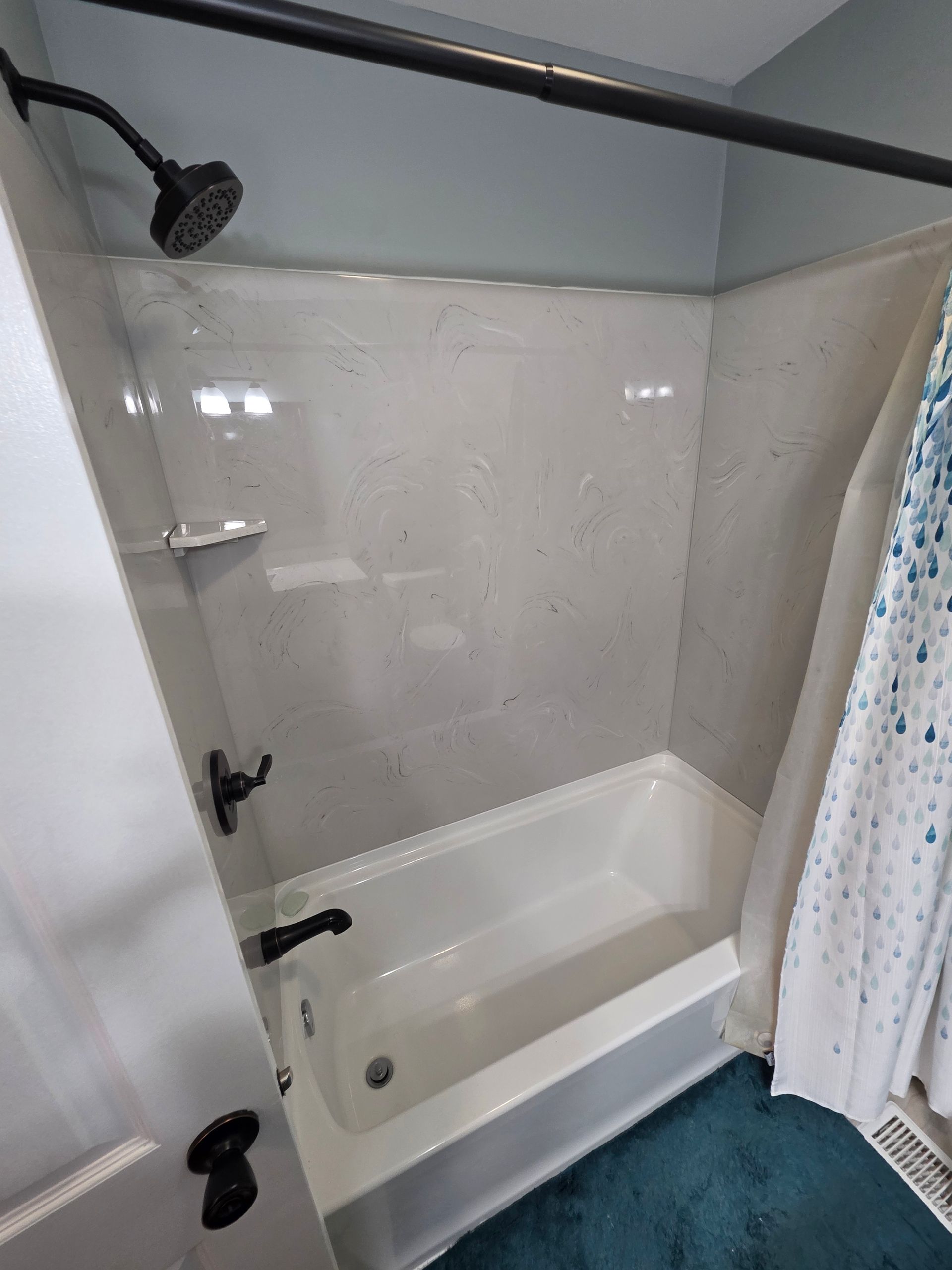 White bathtub and shower with gray speckled walls, black fixtures, and blue shower curtain. | Danville, IL