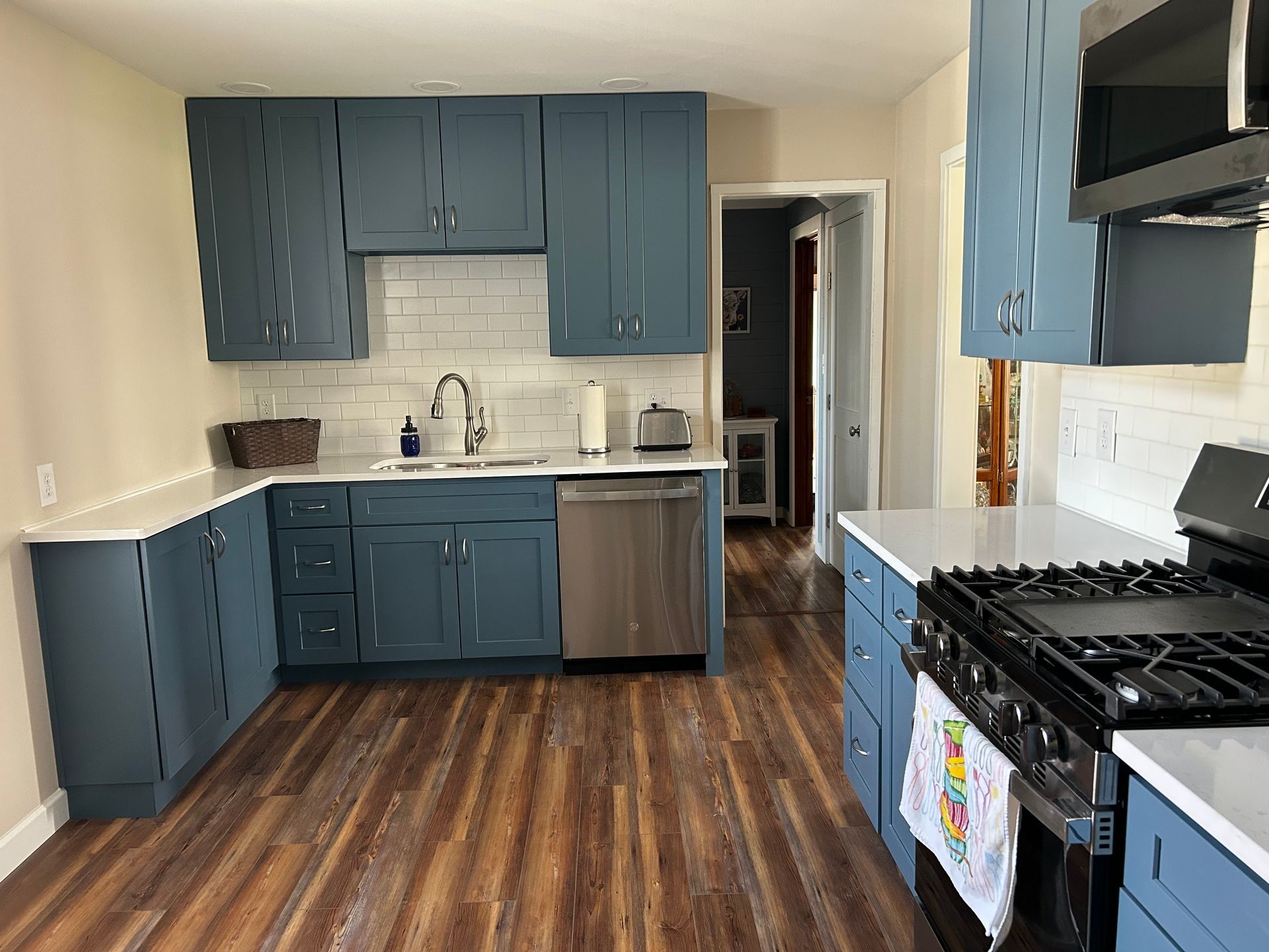 A kitchen with blue cabinets, white countertops, white subway tile backsplash, and wood-patterned flooring. St. Joseph IL