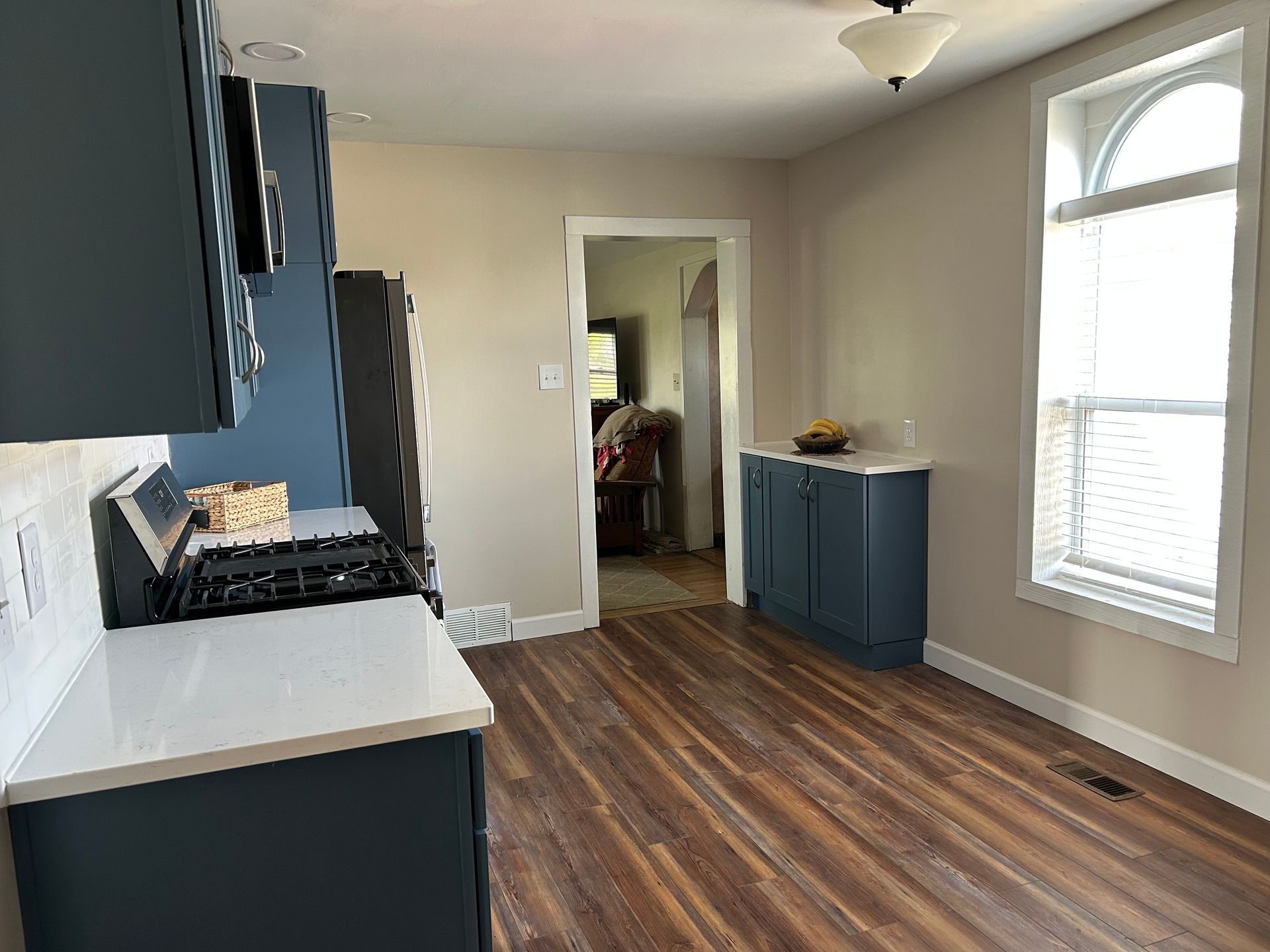A modern kitchen with dark blue cabinets, white countertops, stainless appliances, and wood-look flooring near a window. St. Joseph IL