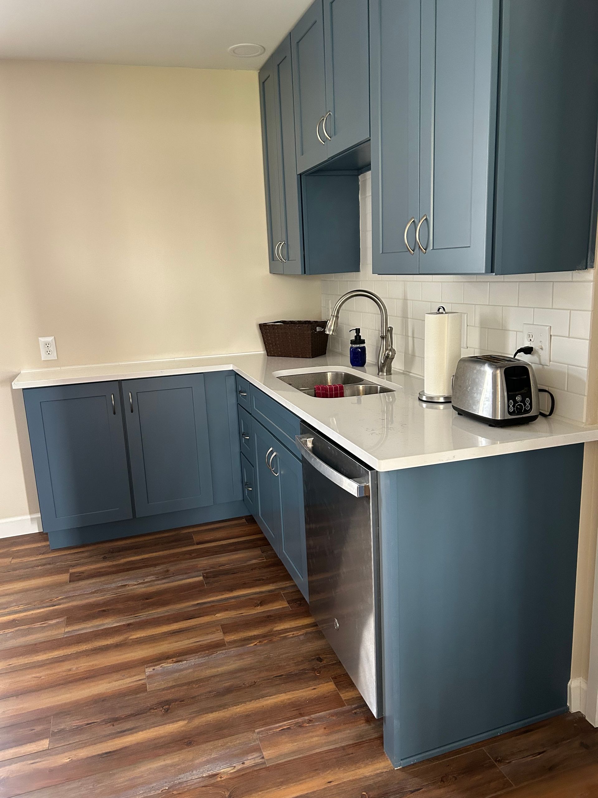 A kitchen corner featuring blue cabinets, white countertops, a sink, and a toaster on wood-look flooring. St. Joseph IL