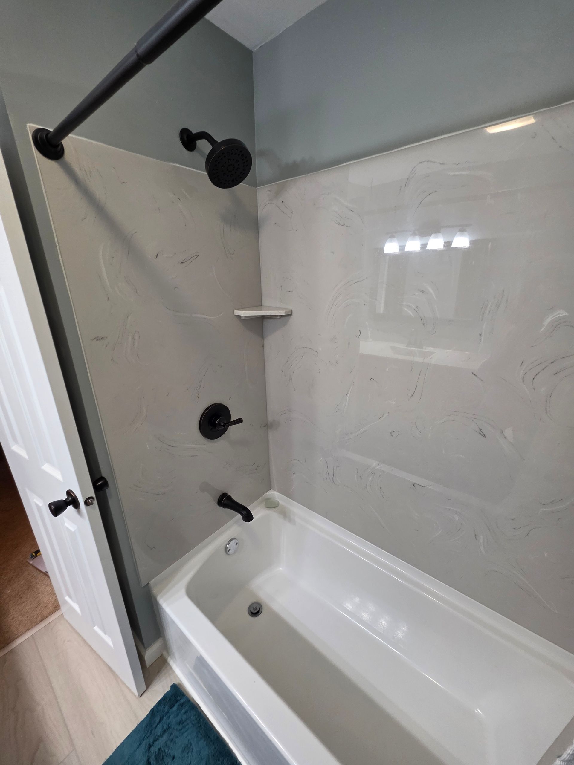A newly remodeled bathroom with a white tub, showerhead, and black fixtures. Gray tile walls and a blue-green painted wall. | Danville, IL