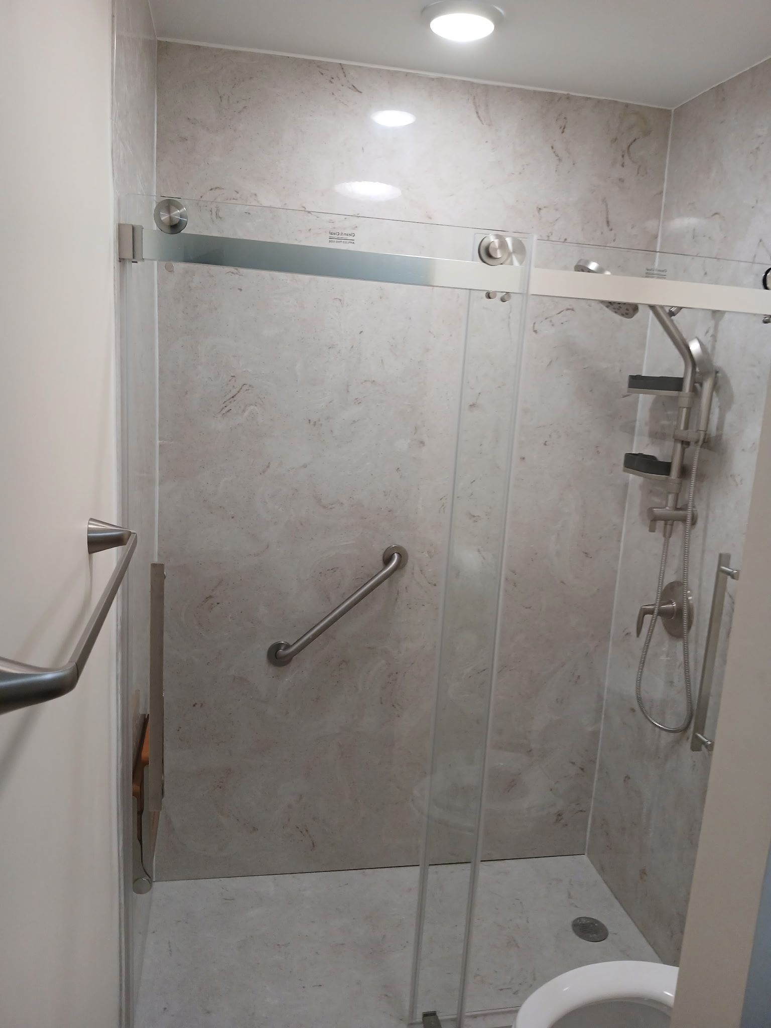 Accessible shower stall with glass door, grab bar, and neutral-colored tile in Danville, IL.