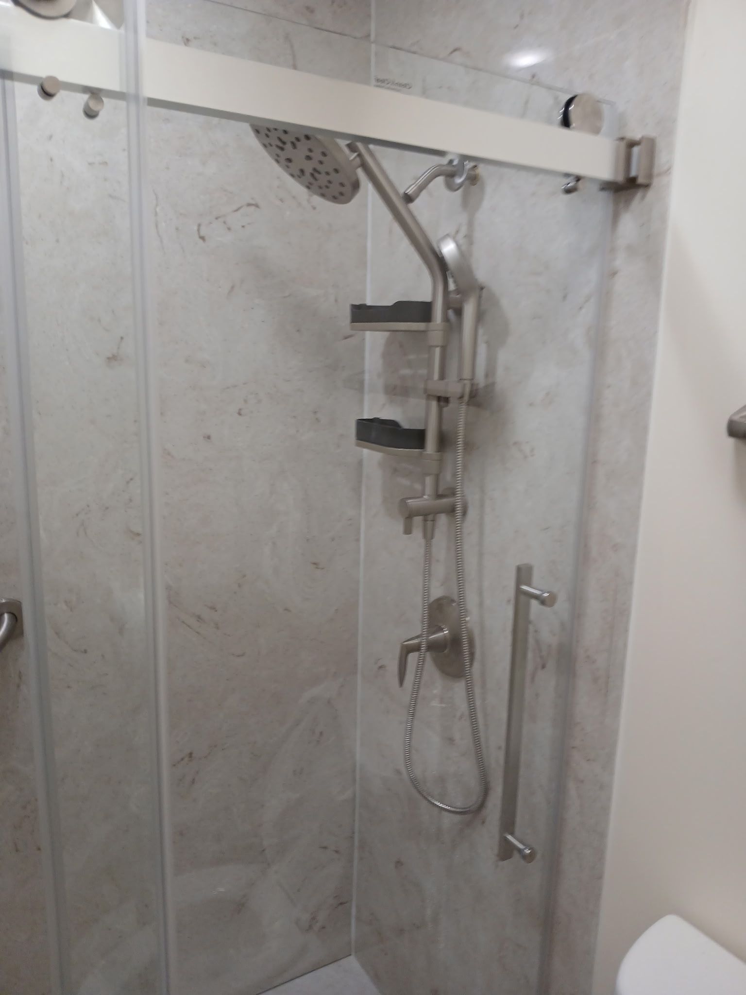Shower with glass doors, silver fixtures, marble-look tile, and a grab bar in Danville, IL
