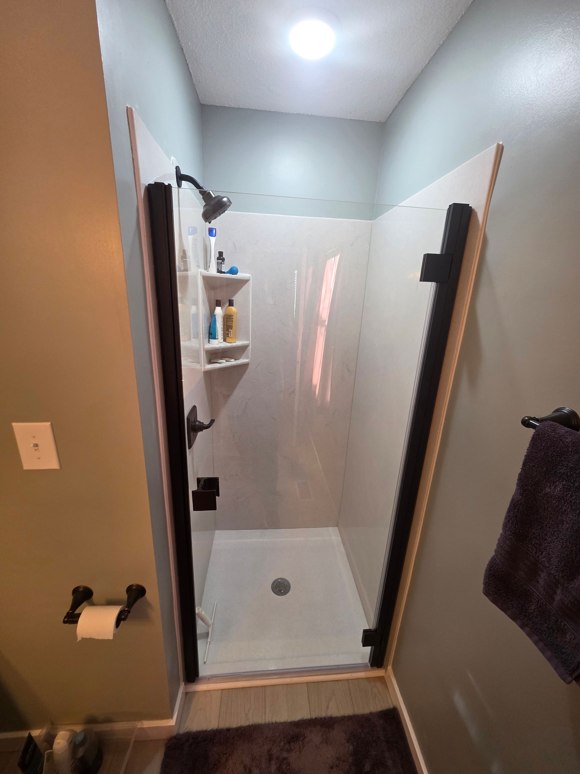 Shower stall with white walls, black frame, shower head, and soap holder.
