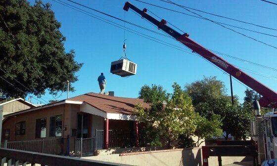 A man is standing on the roof of a house being lifted by a crane